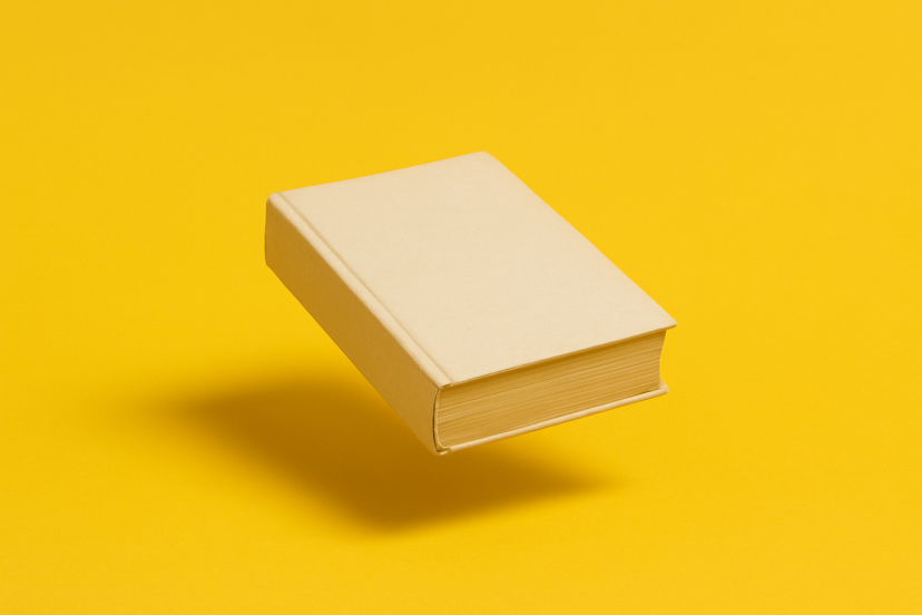 Ein beige eingebundenes Buch schwebt knapp über einem kräftig gelben Hintergrund. Durch den weichen Schatten darunter wirkt es, als würde es leicht in der Luft hängen. Das Buch liegt leicht schräg, die geschlossene Vorderkante zeigt nach rechts.